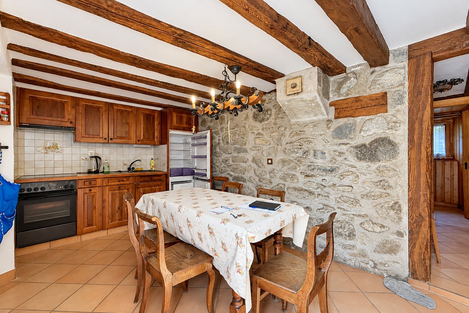 La cuisine en bois massif contre le grand mur de pierre apparente, sous les poutres du plafond.
