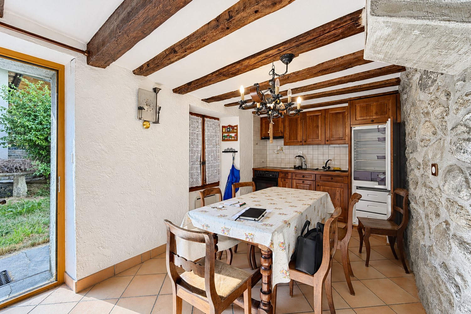 Cuisine-salle à manger de la maison : poutres anciennes, longue table, murs à la chaux et porte vitrée ouvrant sur le jardin.