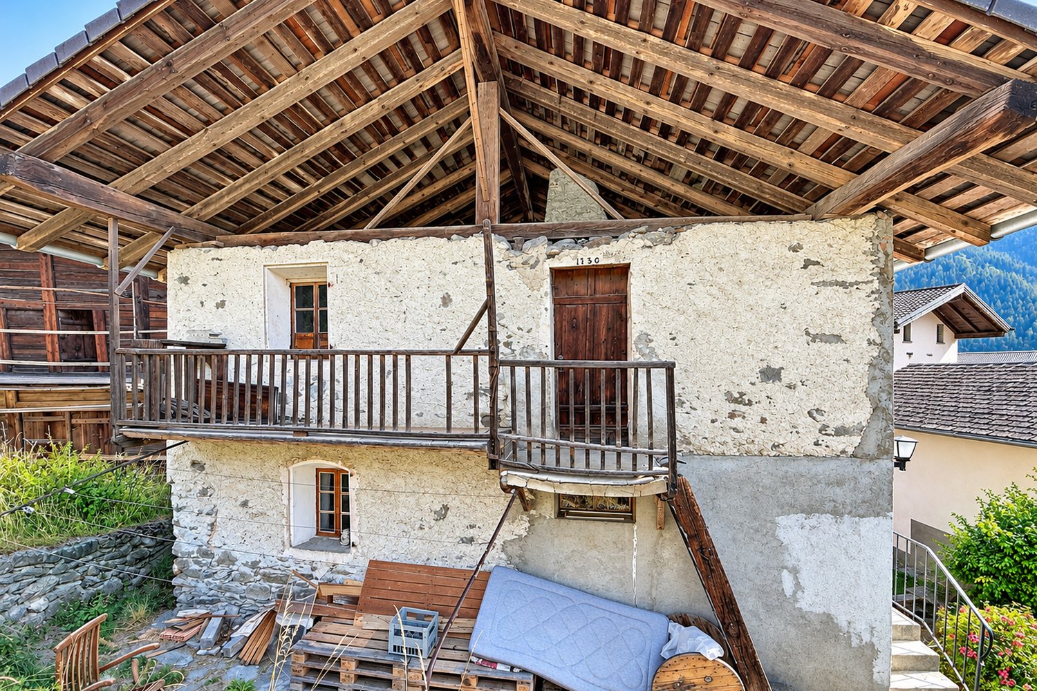 L'arrière de la maison, côté cour : façade maçonnée et balcon ancien sous le grand toit, dans leur état d'origine.